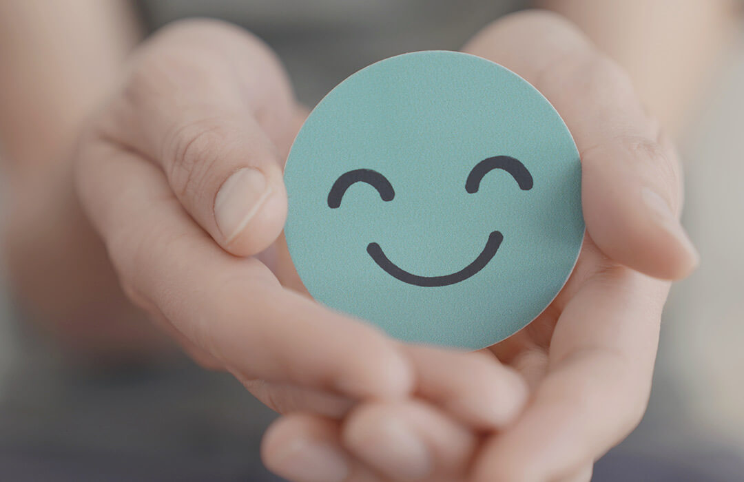 Smiling face badge held in the palm of someone's hands.