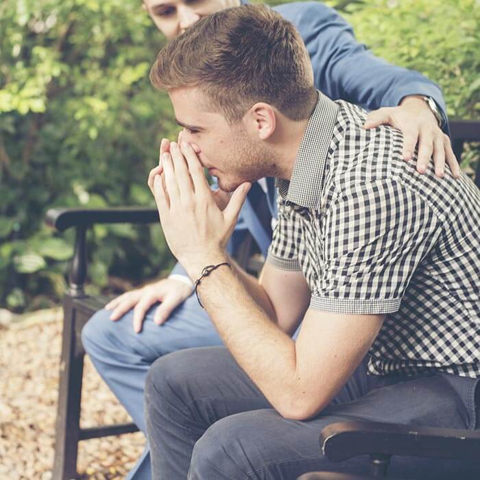 Recovery coach supporting a man on a park bench.