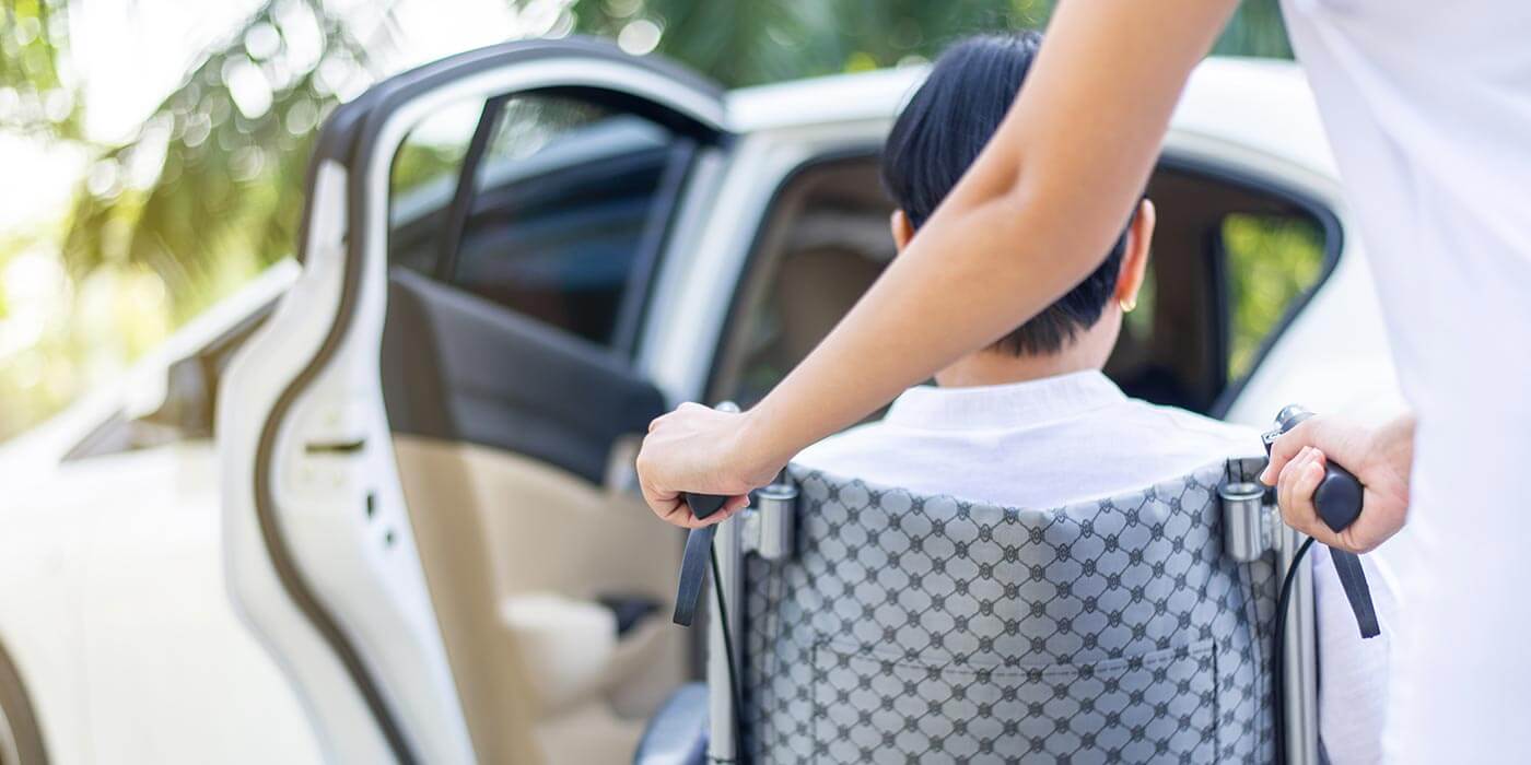 Core support ndis worker helping man into a car with wheelchair.