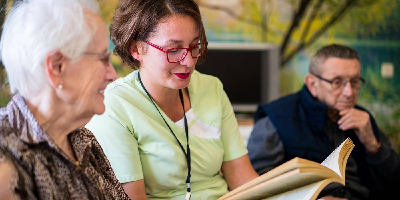 Disability support volunteer reading to an elderly patient.